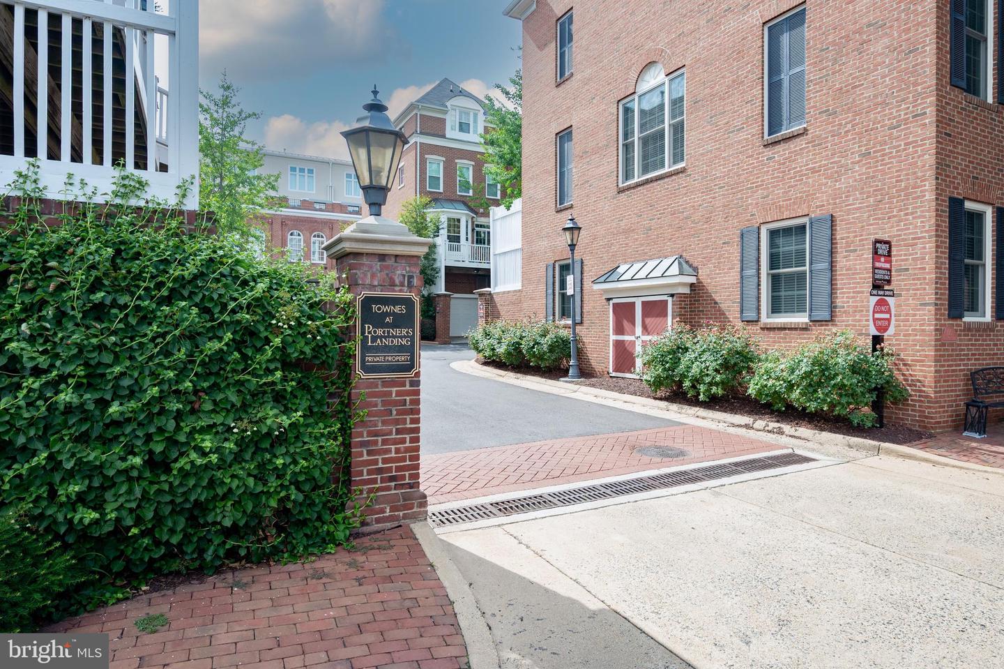 Townhouse community entrance with a brick-paved walkway, hedges, and a lantern-topped sign.