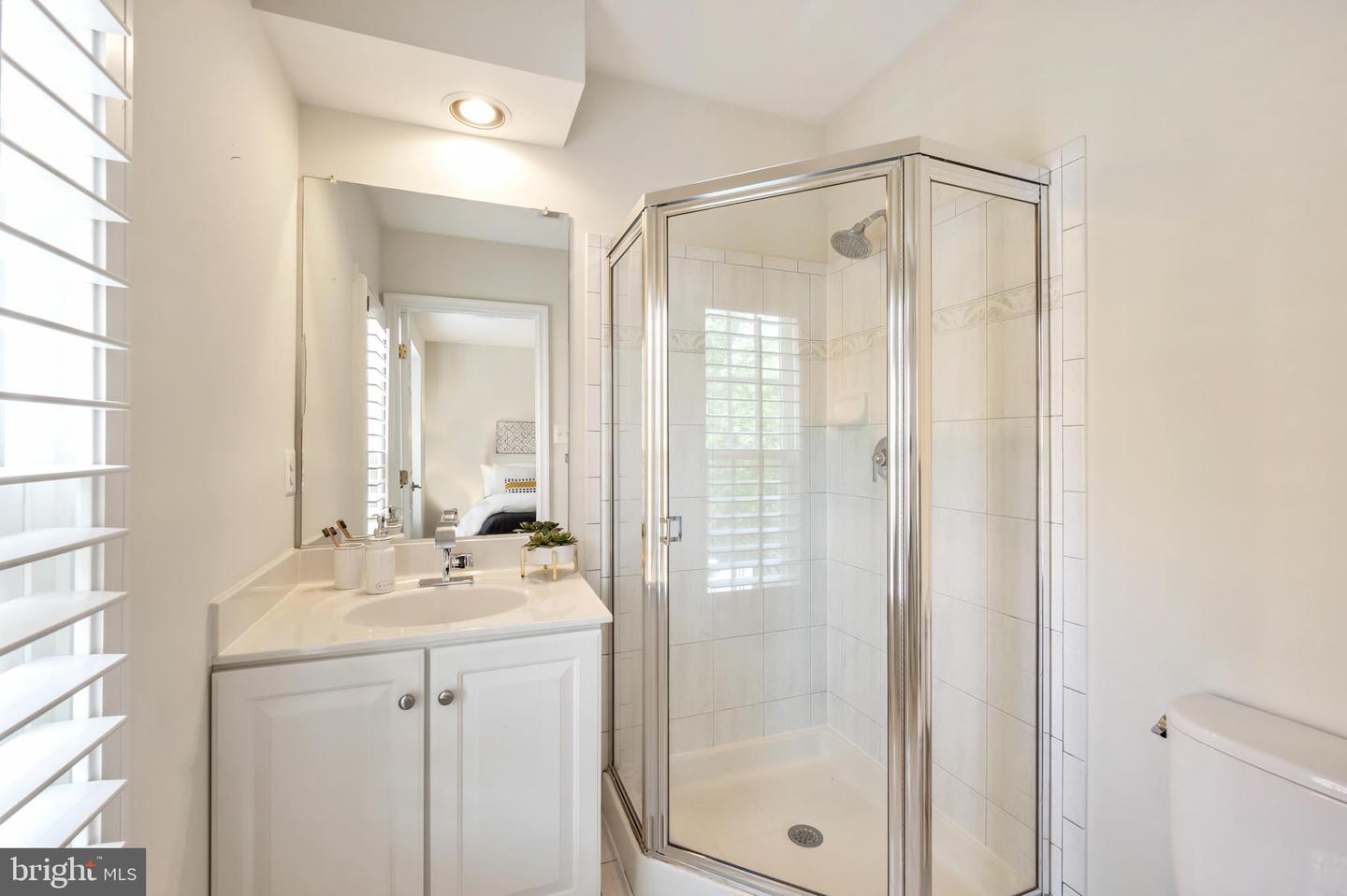 Bathroom with a white vanity, glass-enclosed tiled shower, and plantation shutters.