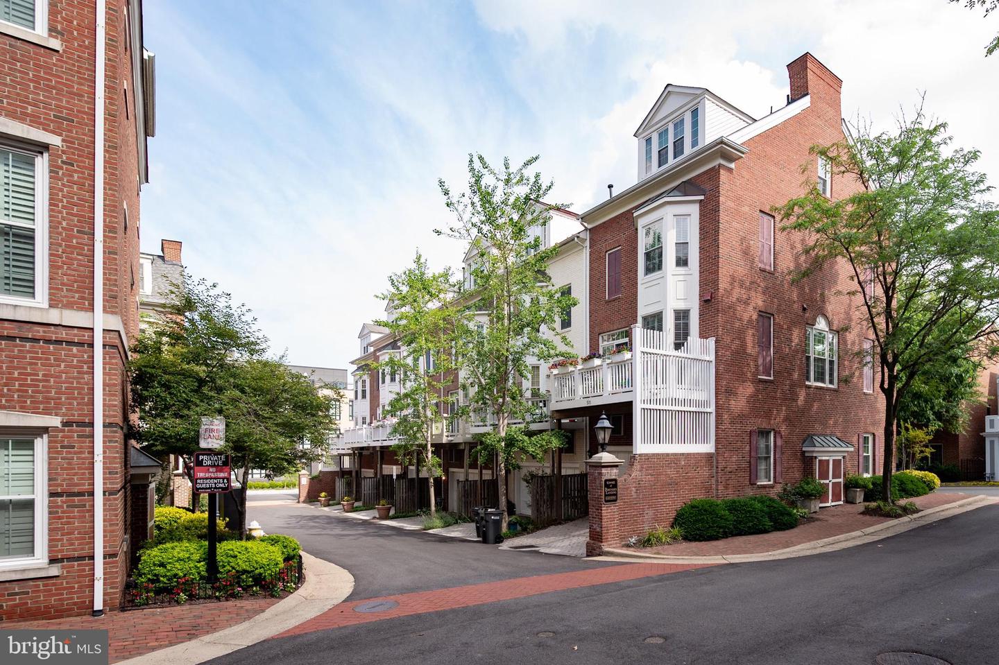 Red-brick townhouse with white balconies and chimney beside a landscaped residential lane.