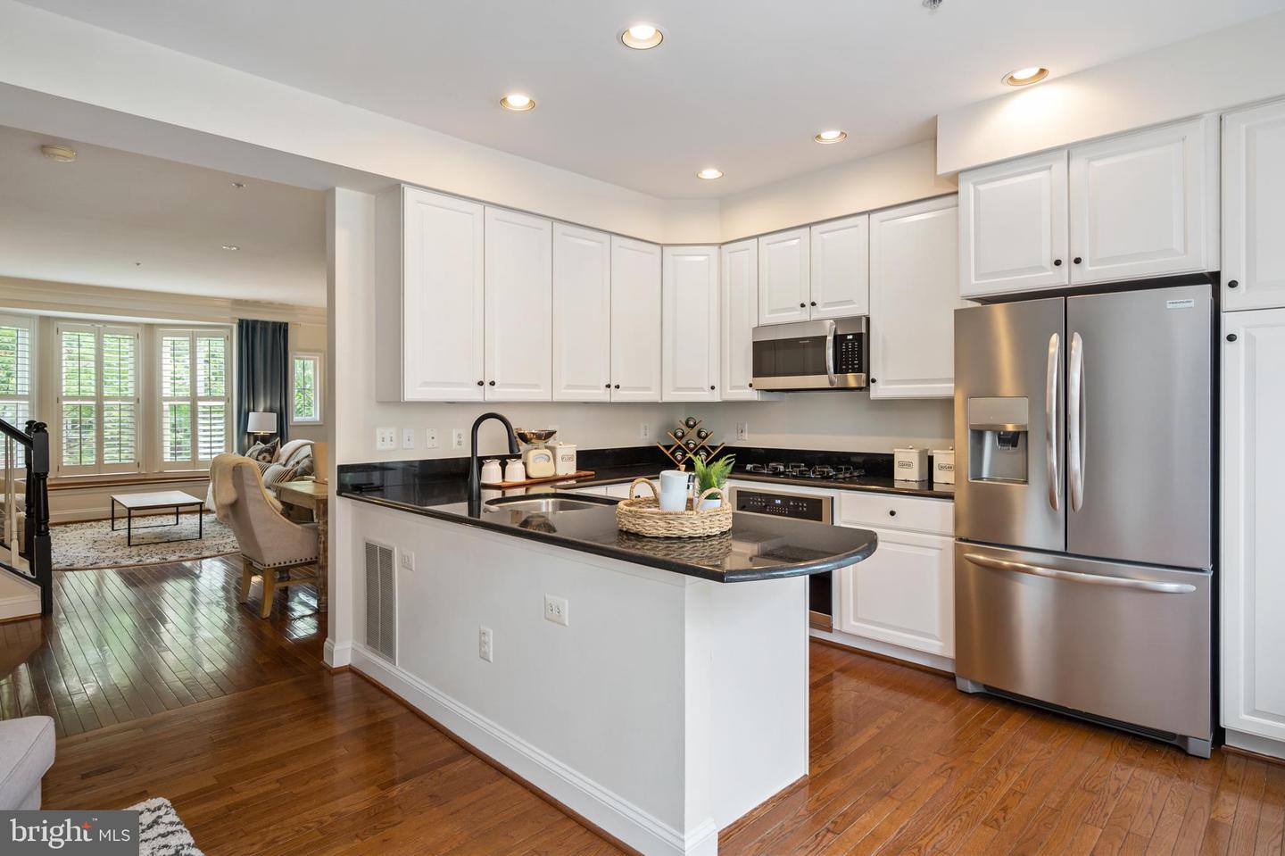 Kitchen with white cabinets, black countertops, a large island, stainless steel appliances, and hardwood floors.