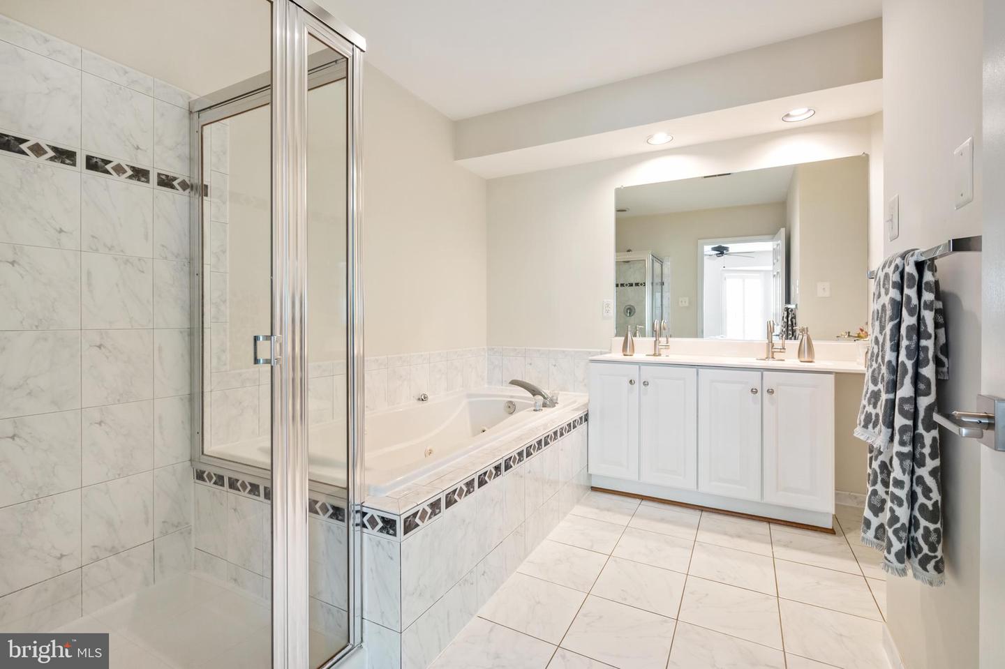 Bathroom with a glass shower, soaking tub, white double vanity, and marble-look tile.