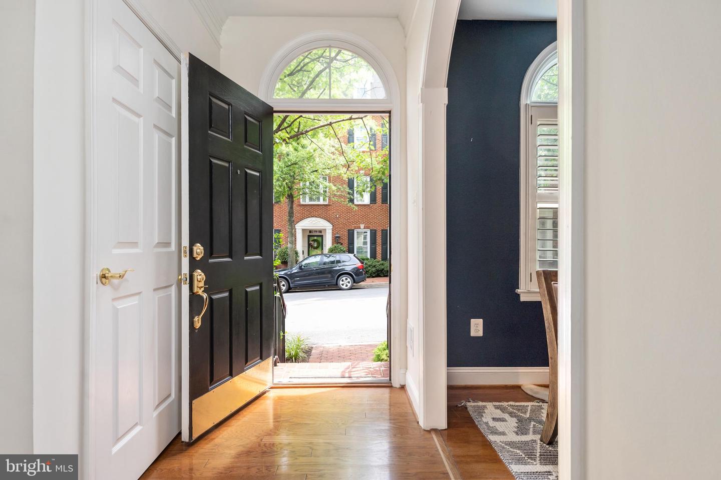 Front entry foyer with an open black door, arched transom window, and hardwood floors.