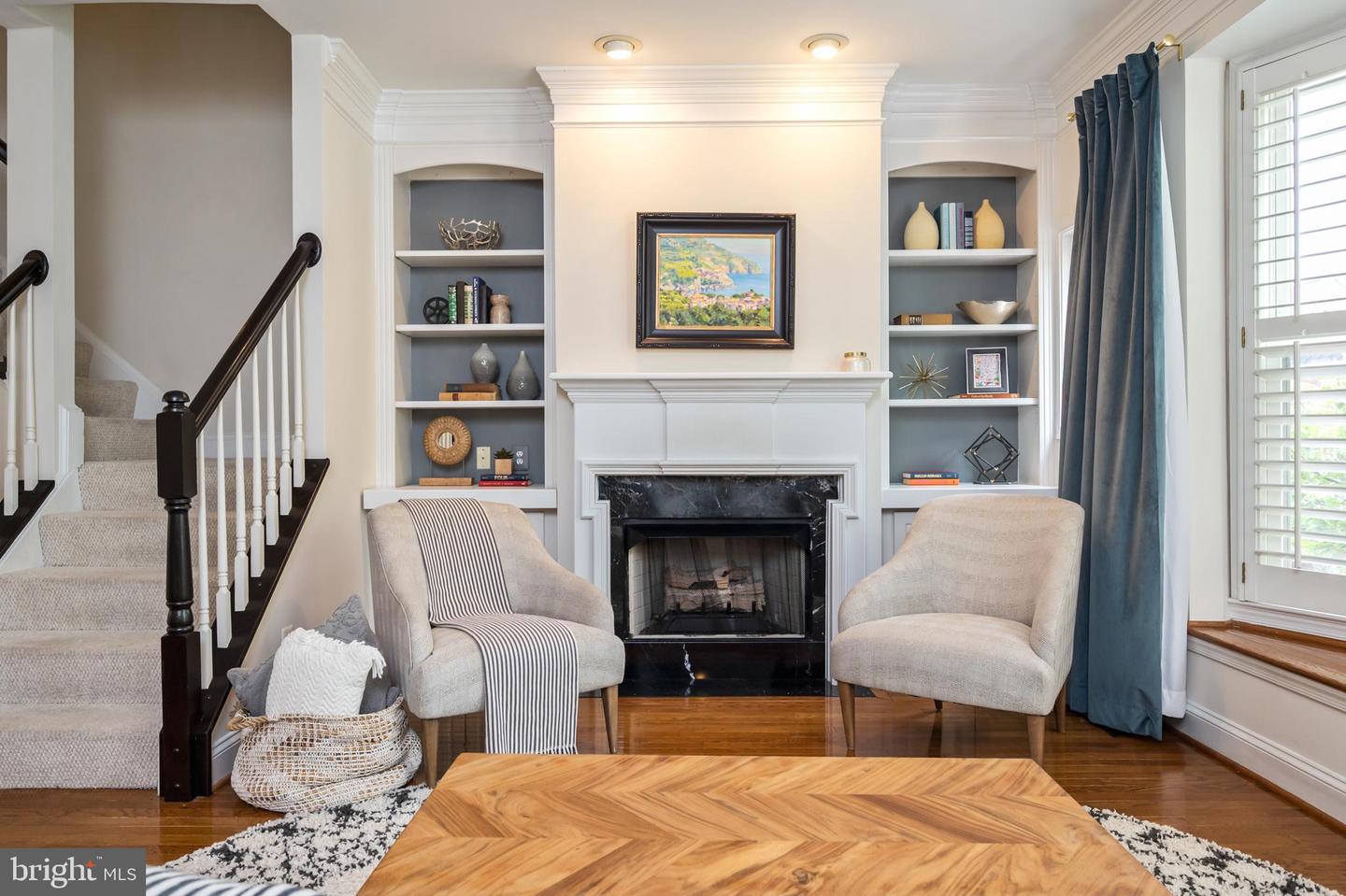 Living room with a white fireplace, built-in shelves, two chairs, and a carpeted staircase.