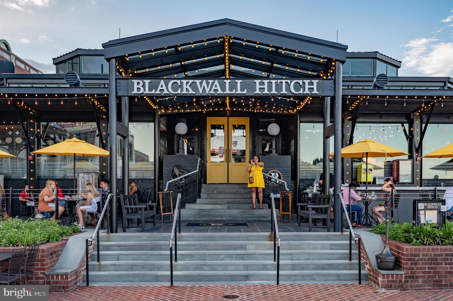 Blackwall Hitch restaurant entrance with a large sign, yellow patio umbrellas, and outdoor diners.