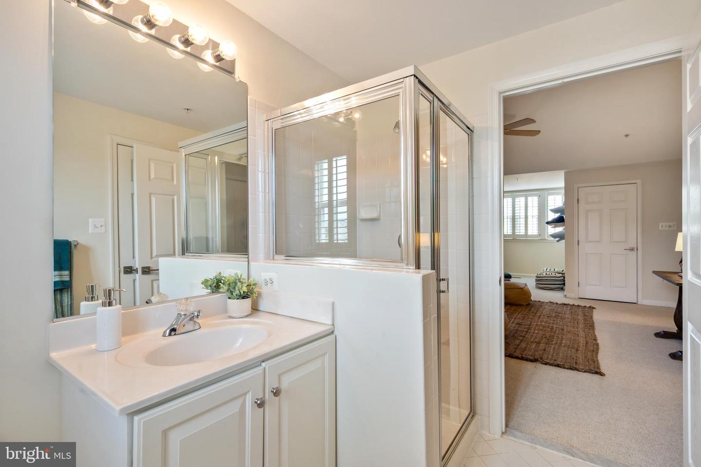 Bathroom with a white vanity and glass shower beside an open doorway to a bedroom.