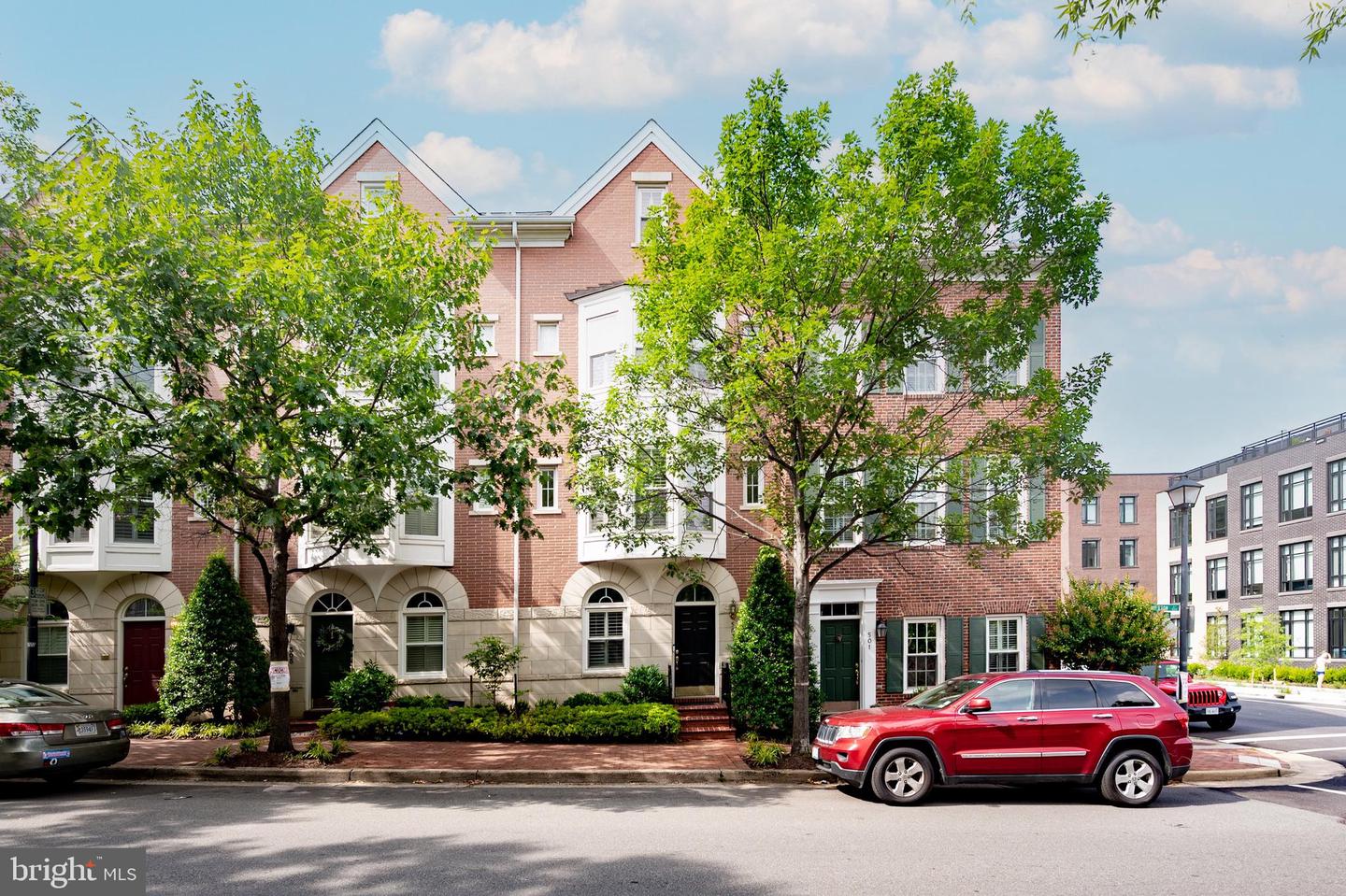Red-brick townhouses with peaked rooflines and bay windows behind leafy street trees.