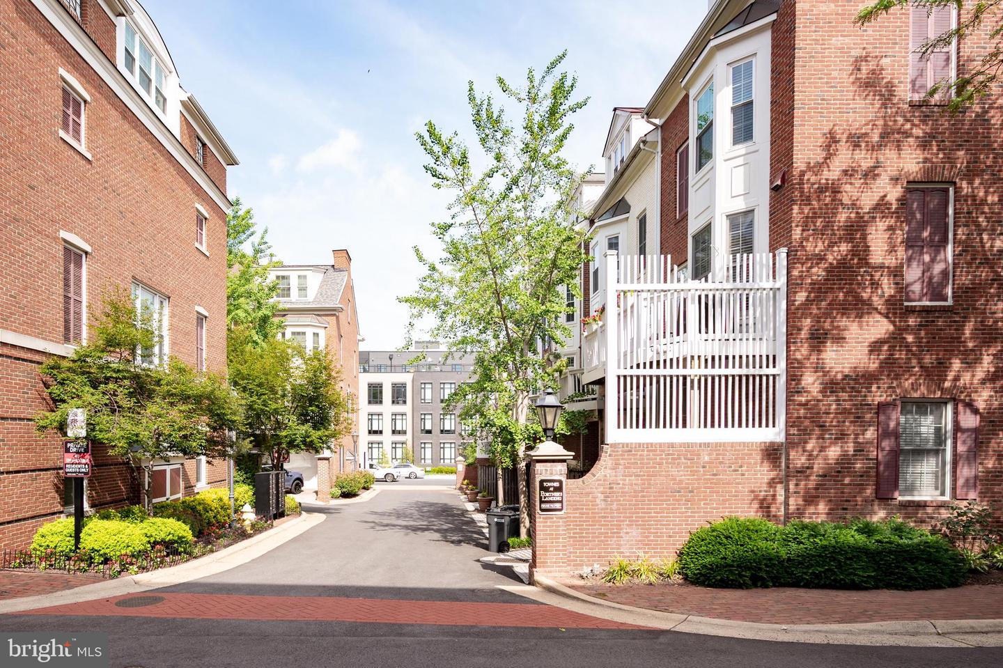 Private drive between red-brick townhomes, with a white-railed balcony and landscaped entrance.