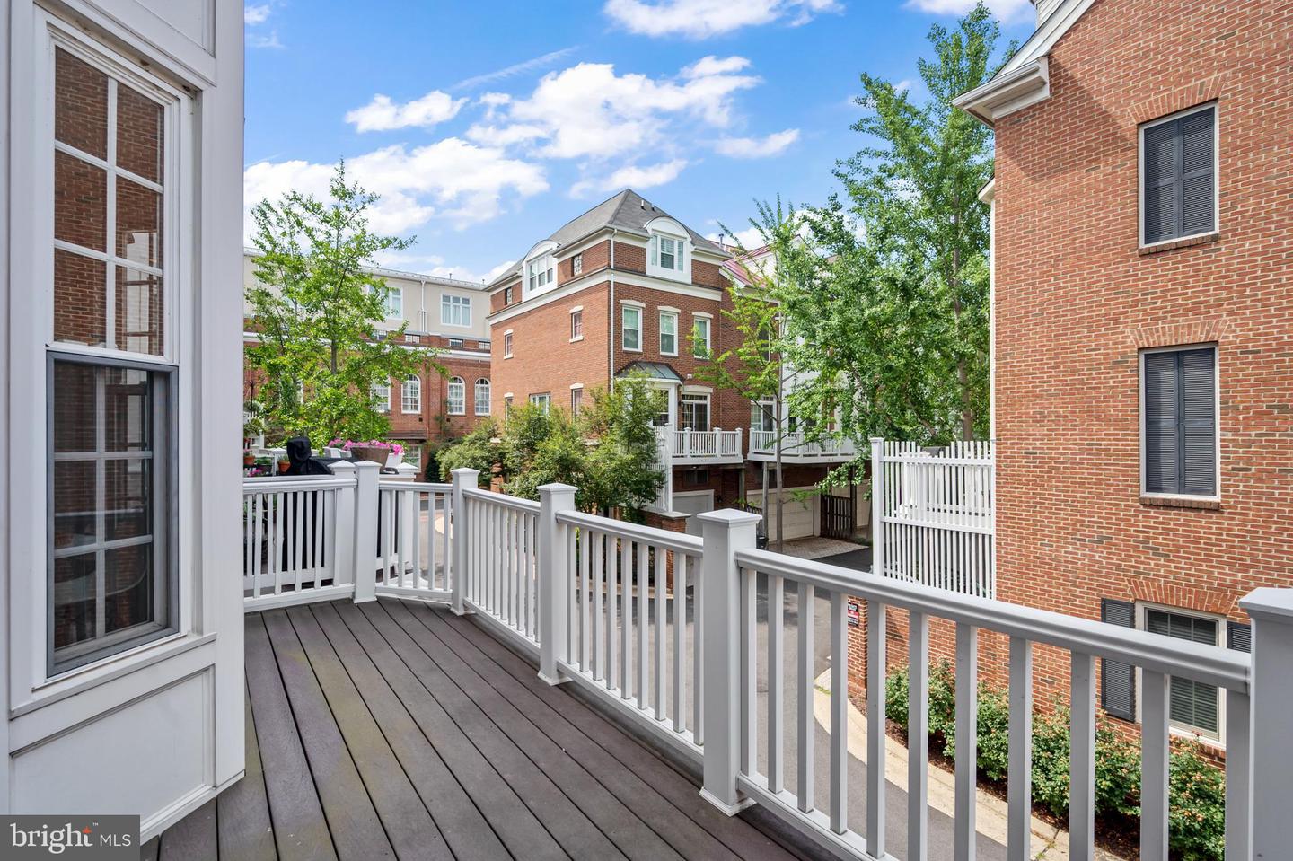 Raised deck with white railings overlooks neighboring brick townhouses and leafy trees.