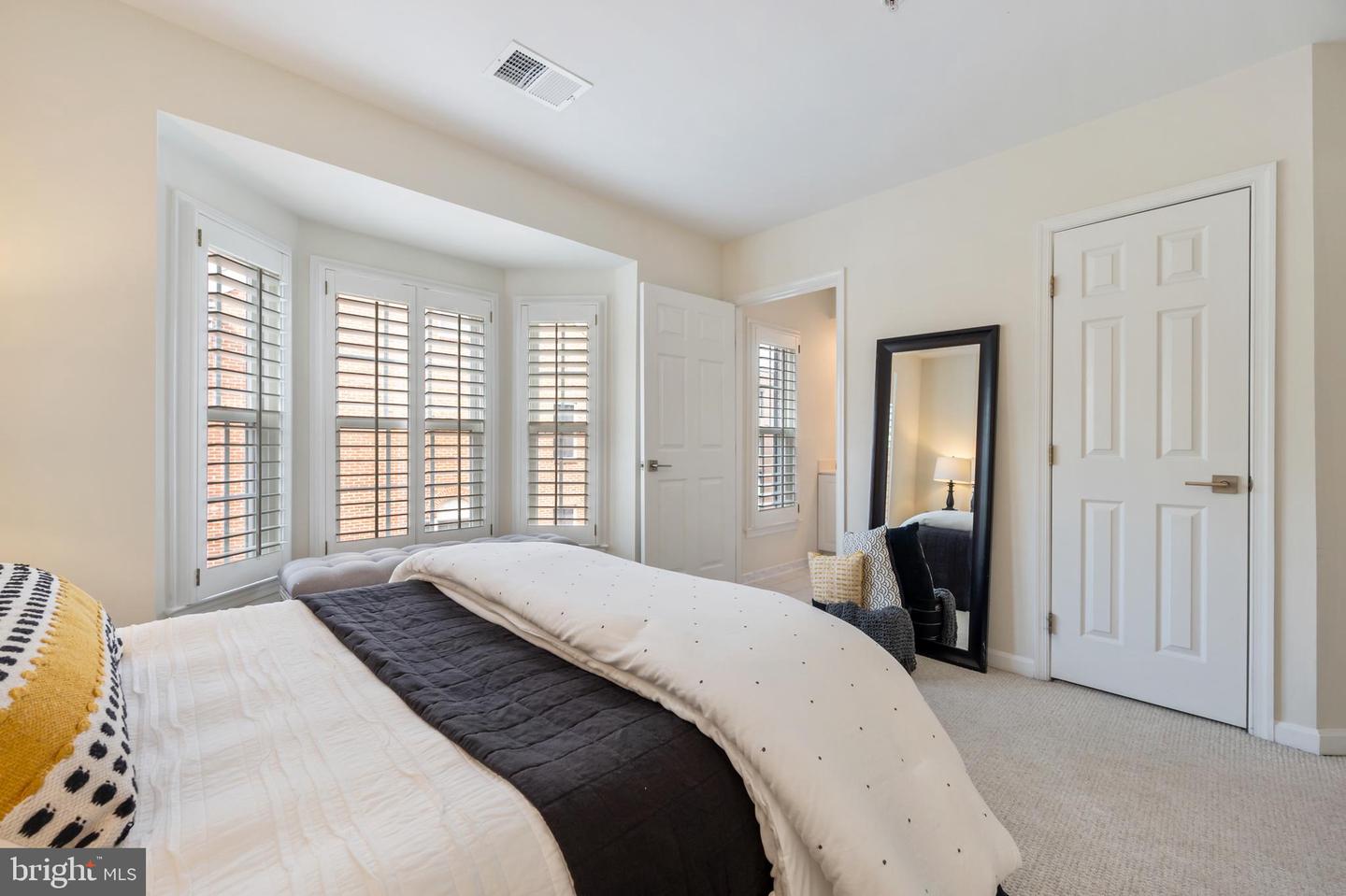 Bedroom with a large bed and tall bay windows fitted with plantation shutters.
