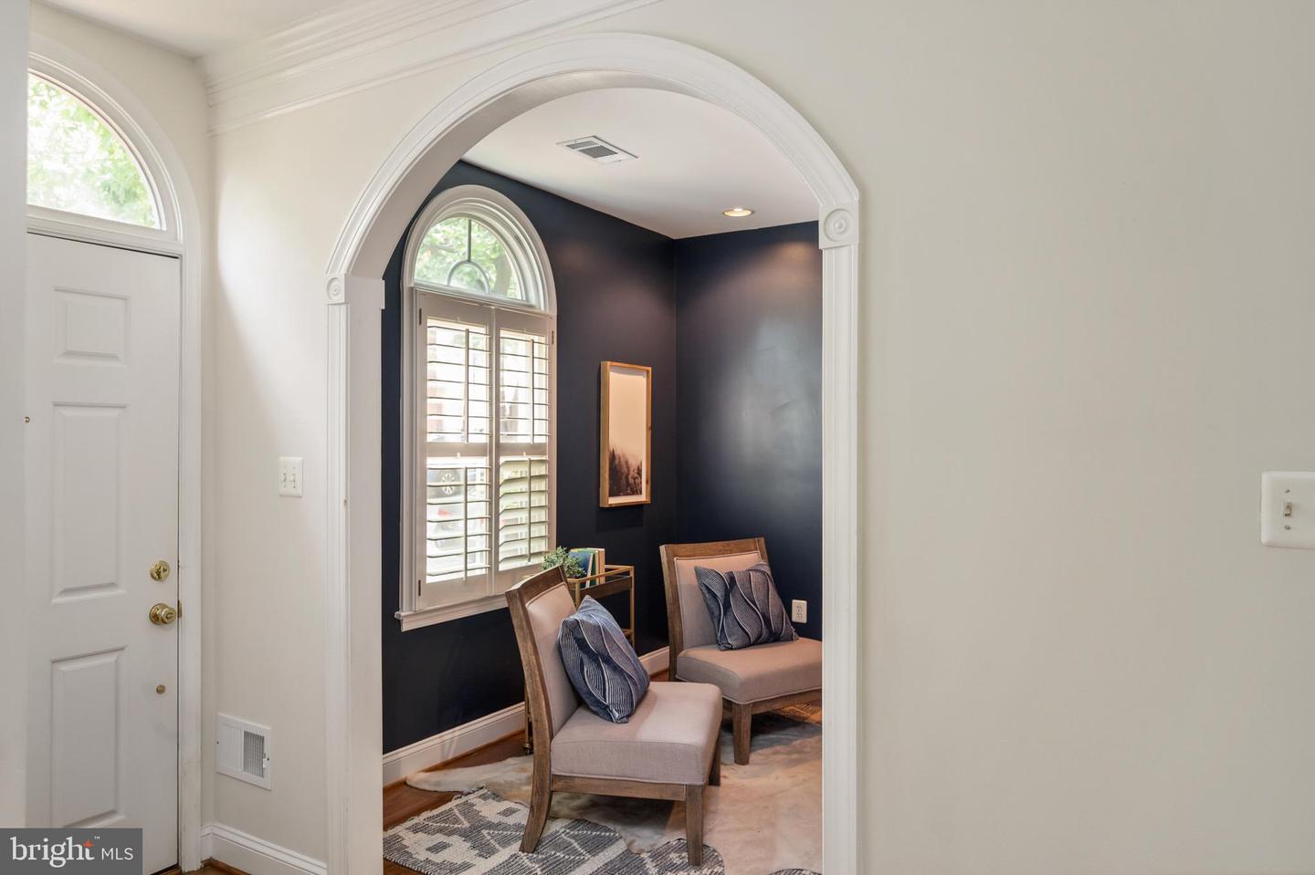 Staged sitting area with two upholstered chairs, navy walls, and an arched shuttered window.