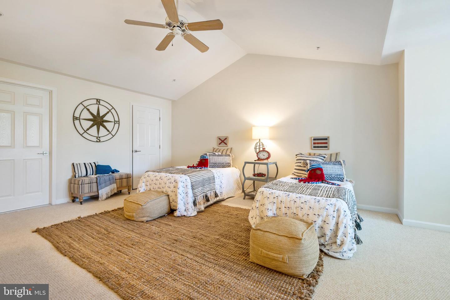 Staged bedroom with two twin beds, a woven rug, and a ceiling fan beneath a vaulted ceiling.