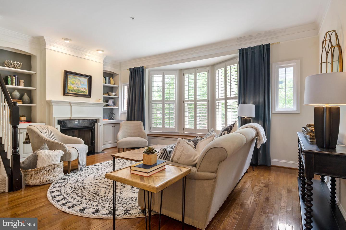 Living room with a fireplace, built-in shelves, shuttered windows, and hardwood floors.