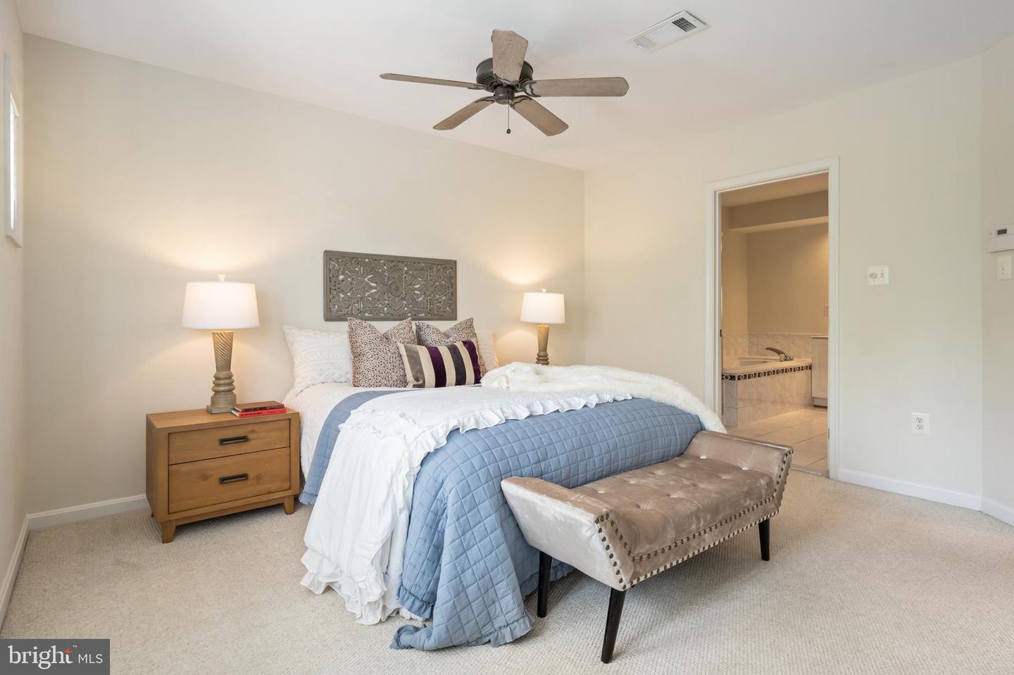 Bedroom with a blue quilted bed, tufted bench, and open doorway to an en-suite bathroom.