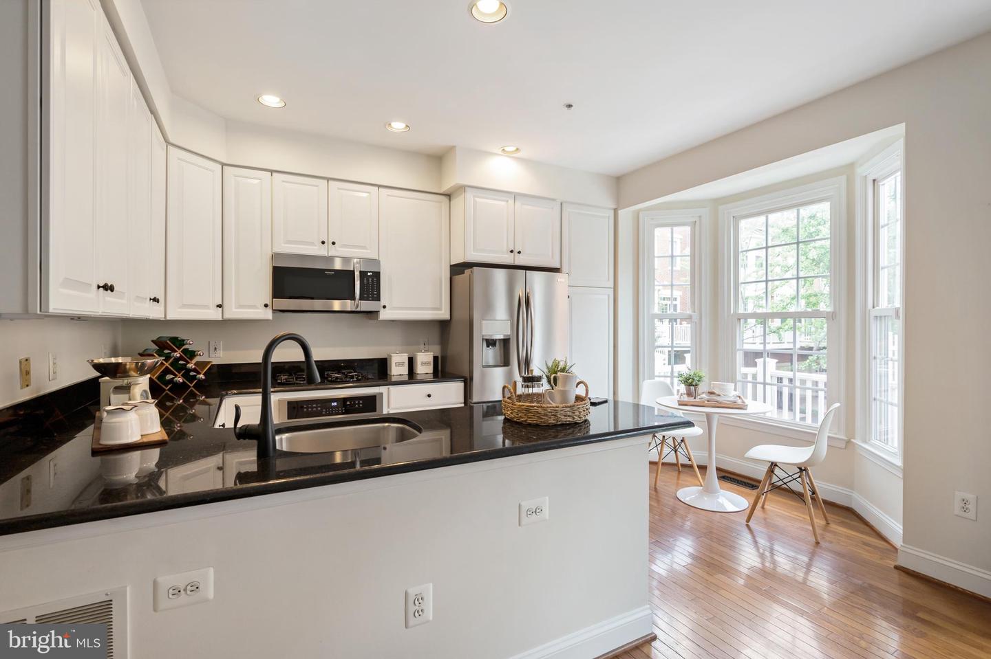 Kitchen with a black-countered island, white cabinets, stainless appliances, and a dining nook by bay windows.