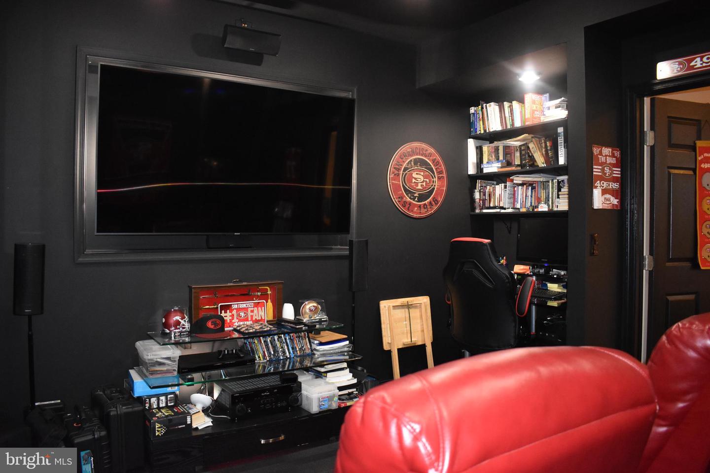 Media room with a large television, 49ers memorabilia, book shelves, and a red leather sofa.