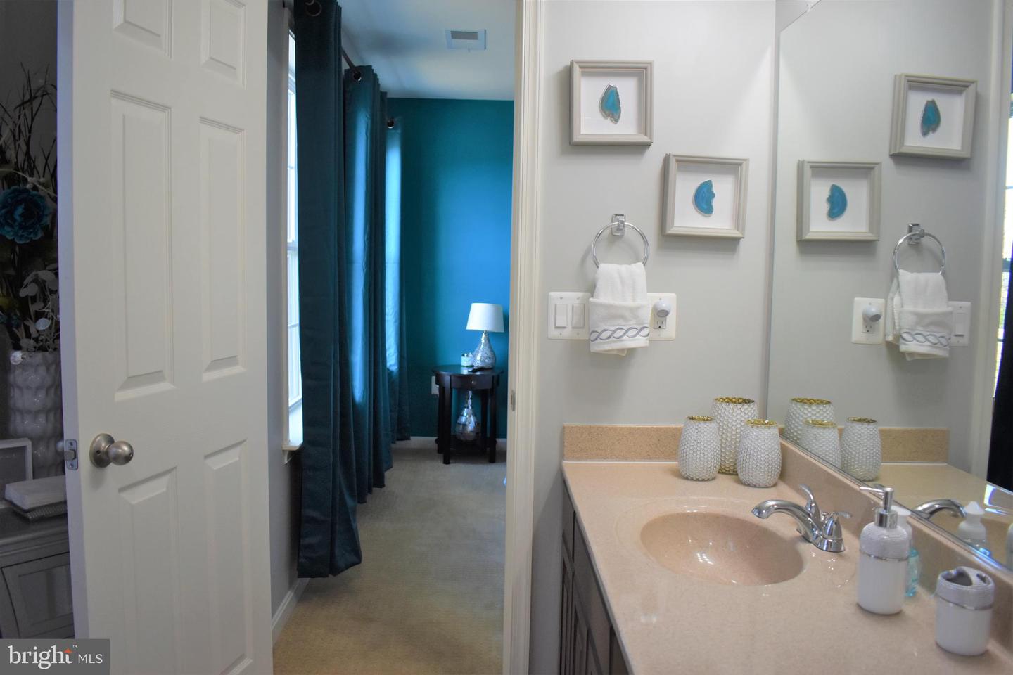 Bathroom vanity with a beige countertop and large mirror, beside an open doorway to a teal room.