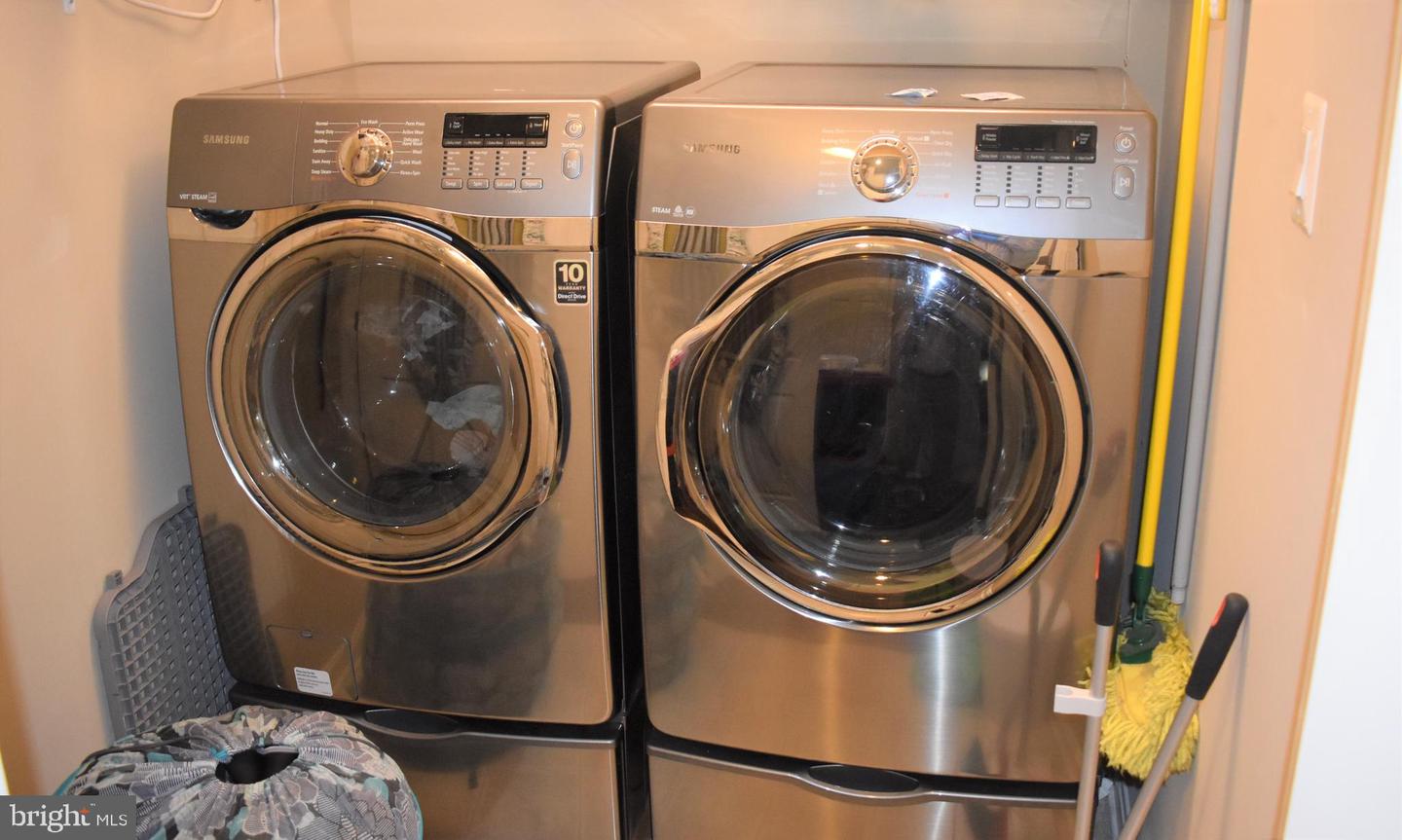 Laundry room with matching stainless steel front-loading washer and dryer and cleaning tools.