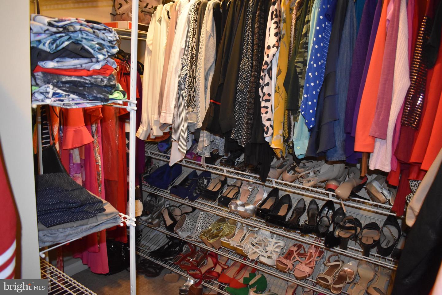 Walk-in closet with colorful hanging clothes, folded garments, and shoes on wire racks.