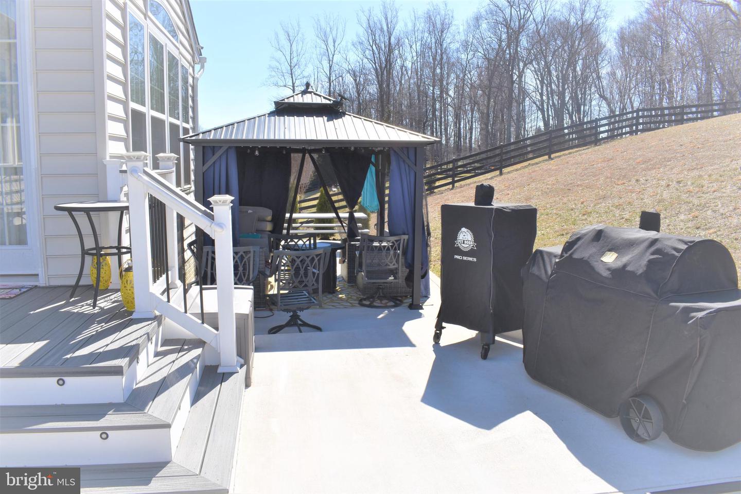 Patio with a curtained gazebo, raised deck, and covered grills beside the house.