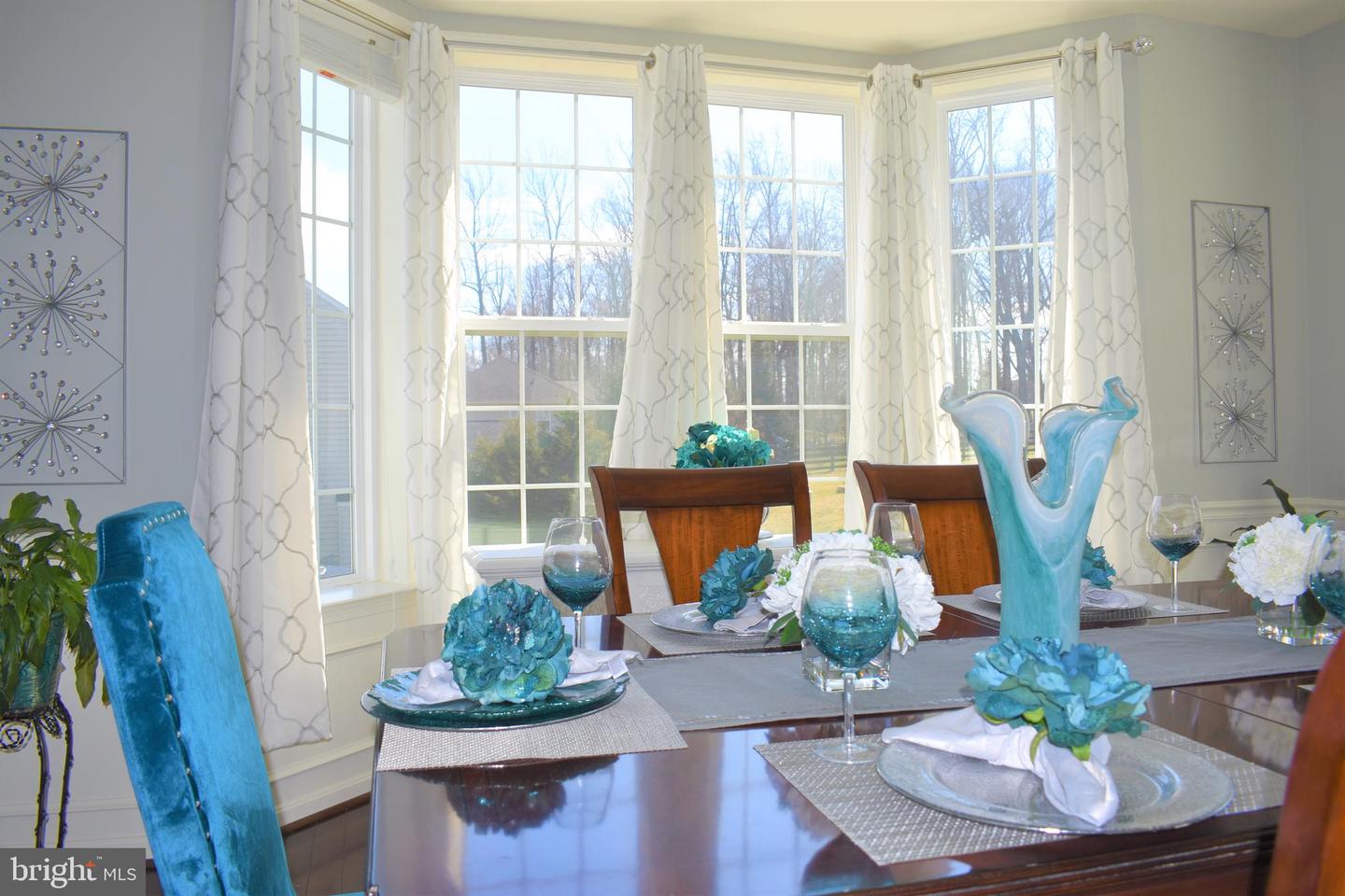 Staged dining room with a dark wood table, turquoise place settings, and tall windows overlooking leafless trees.