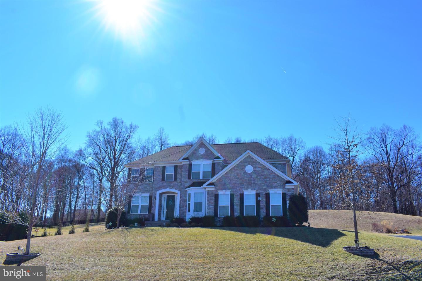 Two-story stone-front house with white trim on a sloping lawn, framed by leafless trees.