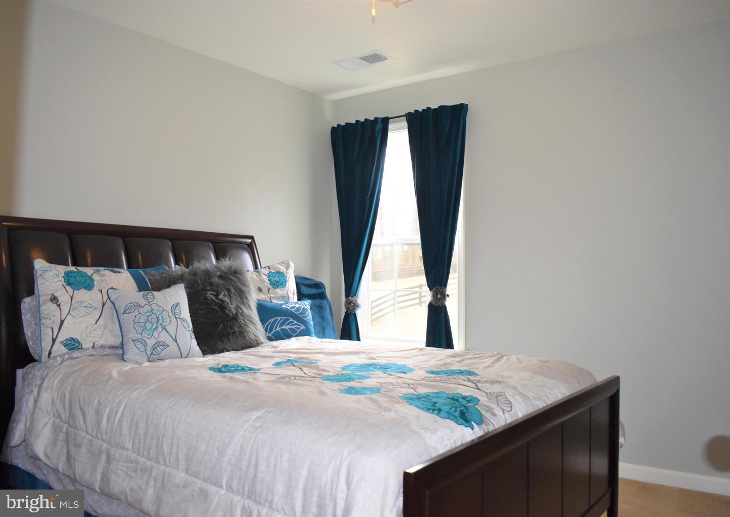 Furnished bedroom with a dark wood bed, turquoise floral bedding, and teal curtains.