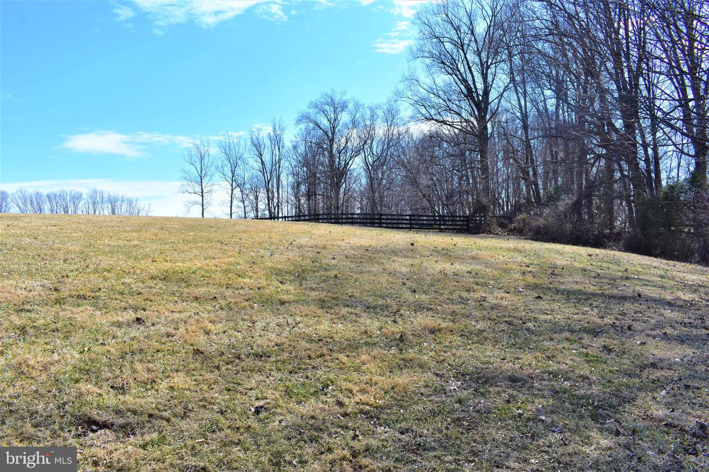 Open grassy lot with a black rail fence and leafless trees along its edge.