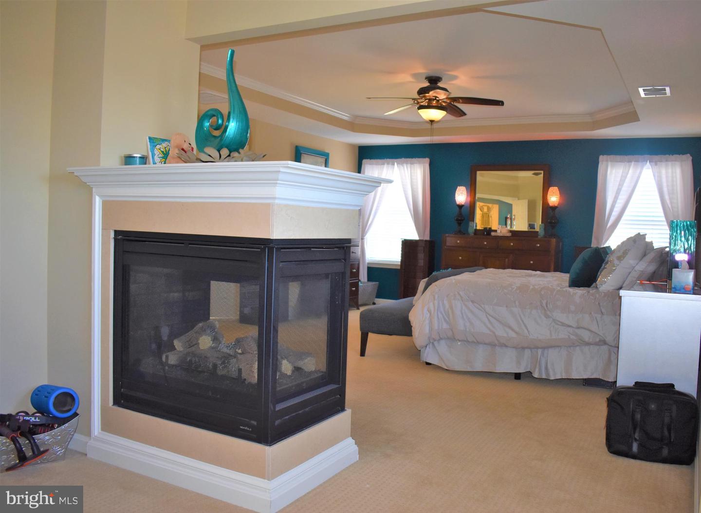 Bedroom with a bed, teal accent wall, ceiling fan, and prominent two-sided fireplace.