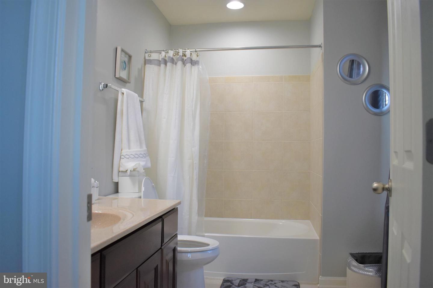 Bathroom with a beige tiled tub surround, white shower curtain, and dark vanity.
