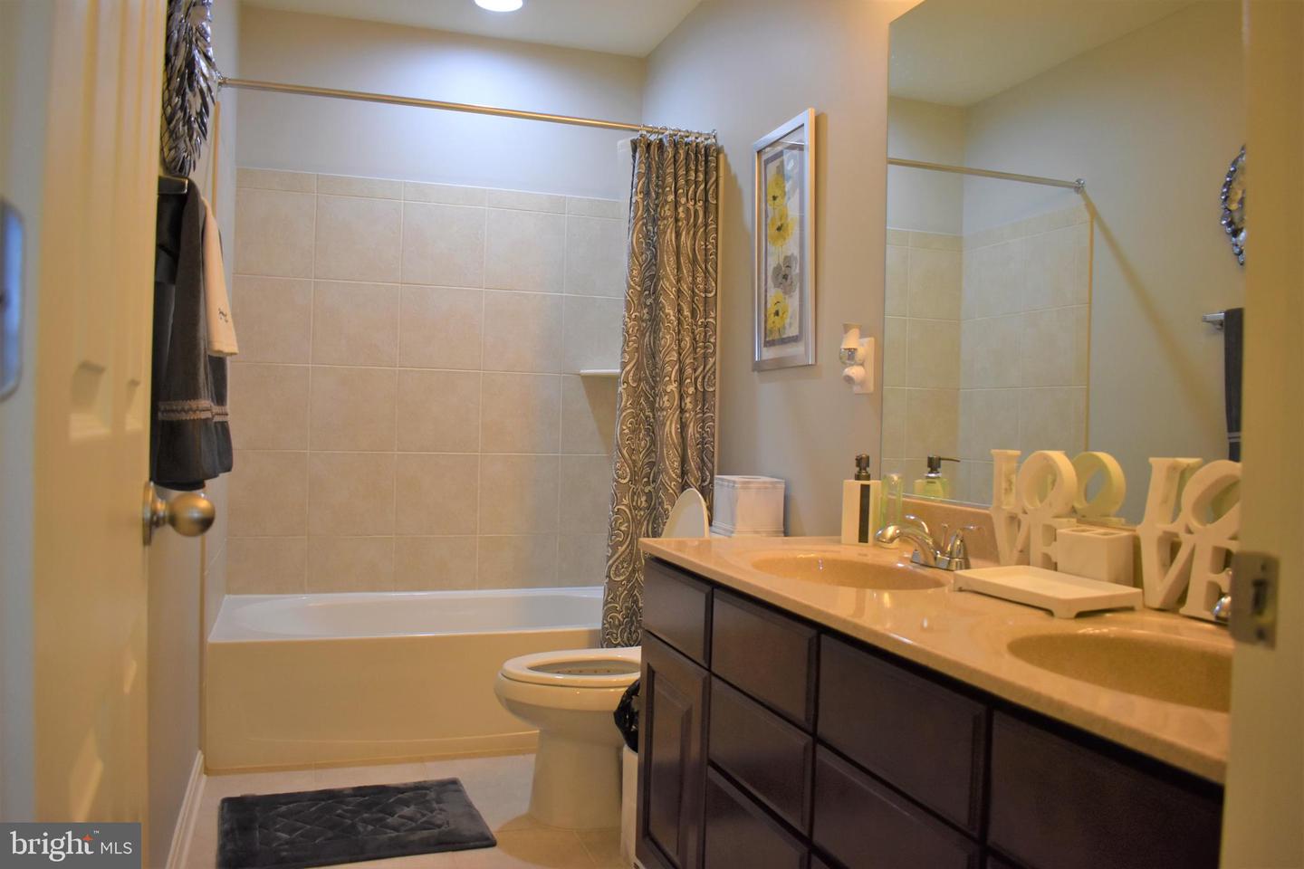 Bathroom with a bathtub and patterned curtain beside a dark double-sink vanity.
