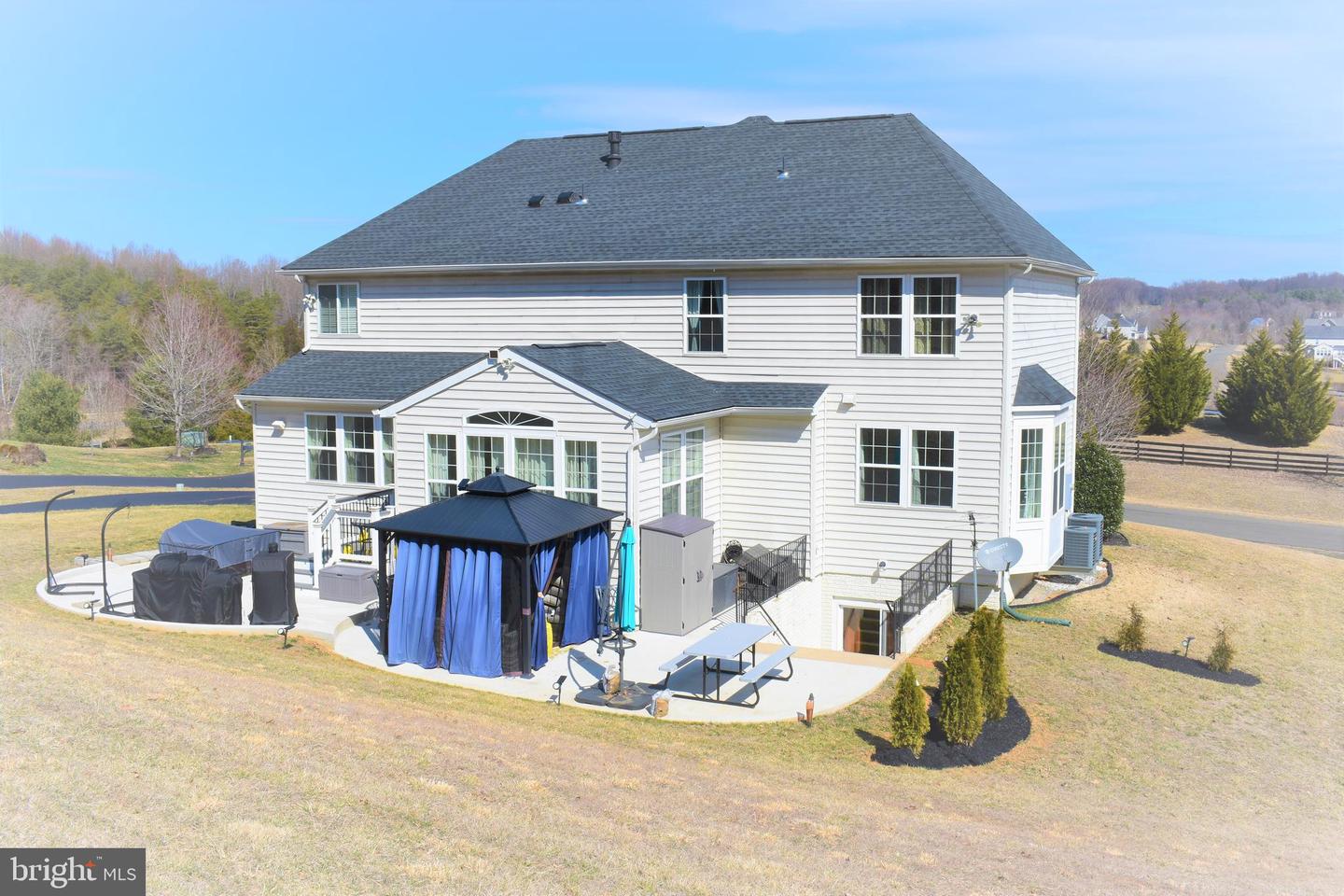 Rear of a two-story white house with a blue-curtained gazebo on the patio.