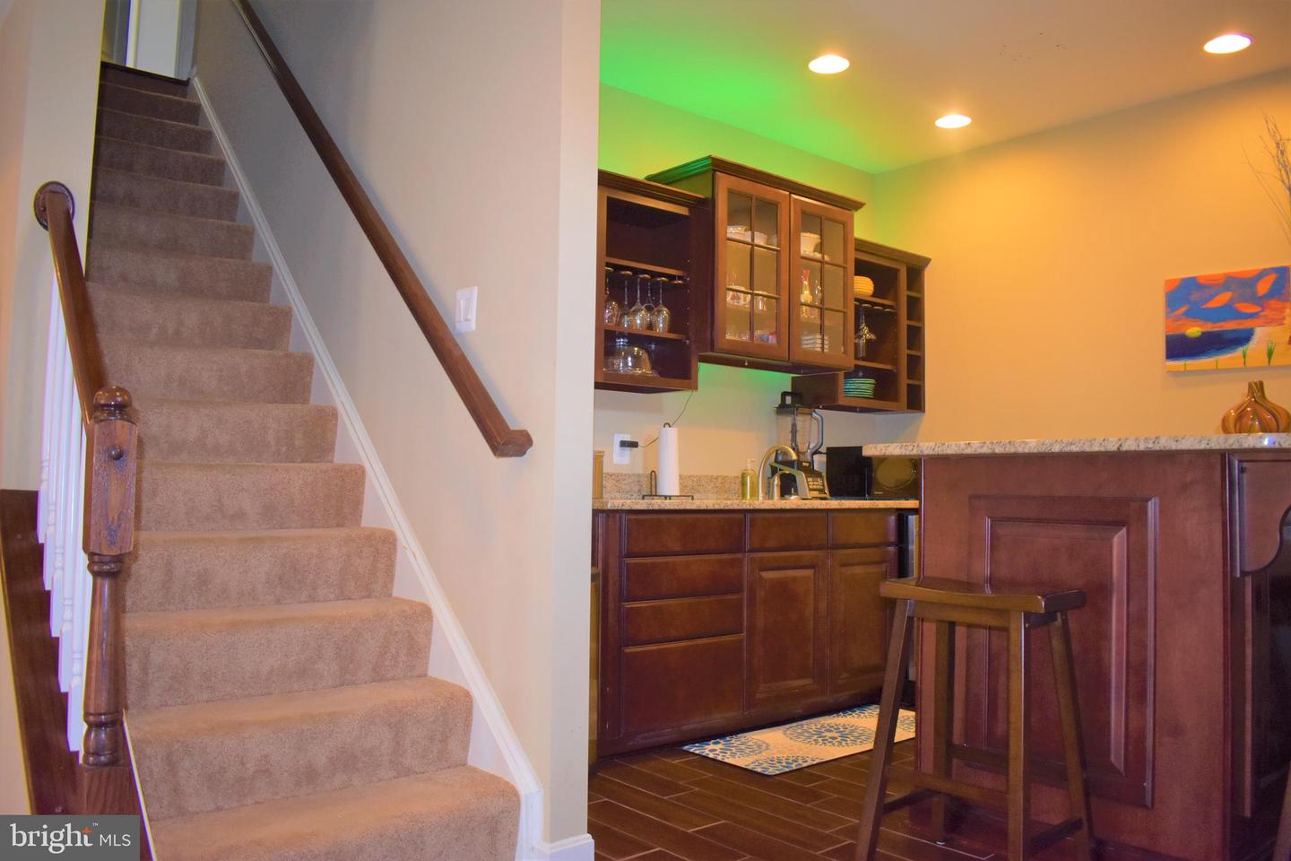 Kitchen and bar with dark wood cabinetry and granite counters beside a carpeted staircase.