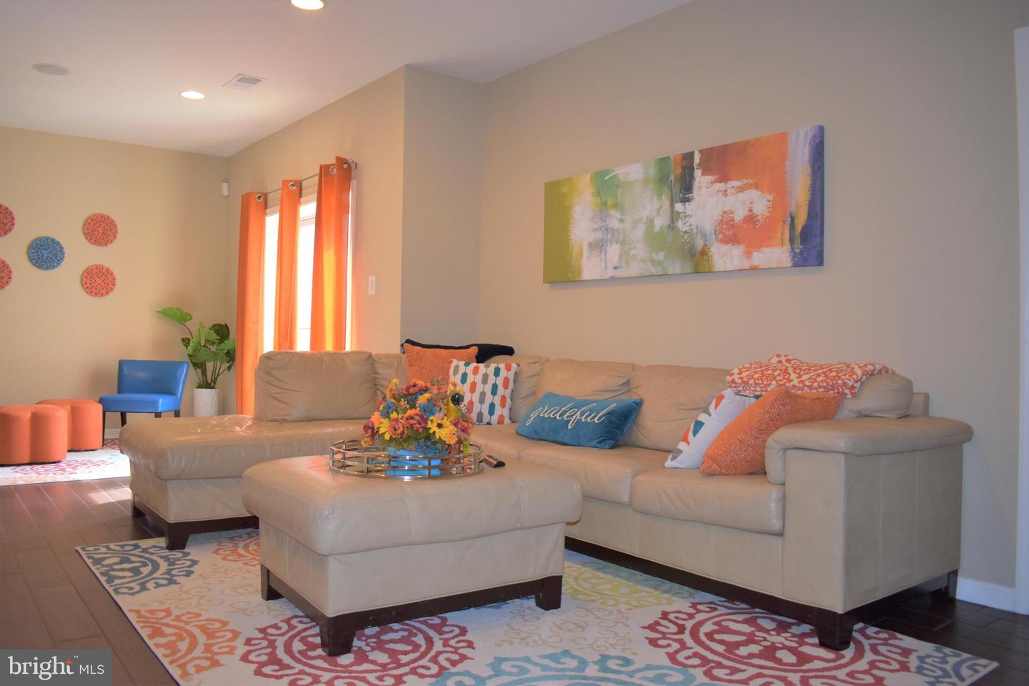 Furnished living room with a beige sectional, colorful patterned rug, and bright orange curtains.