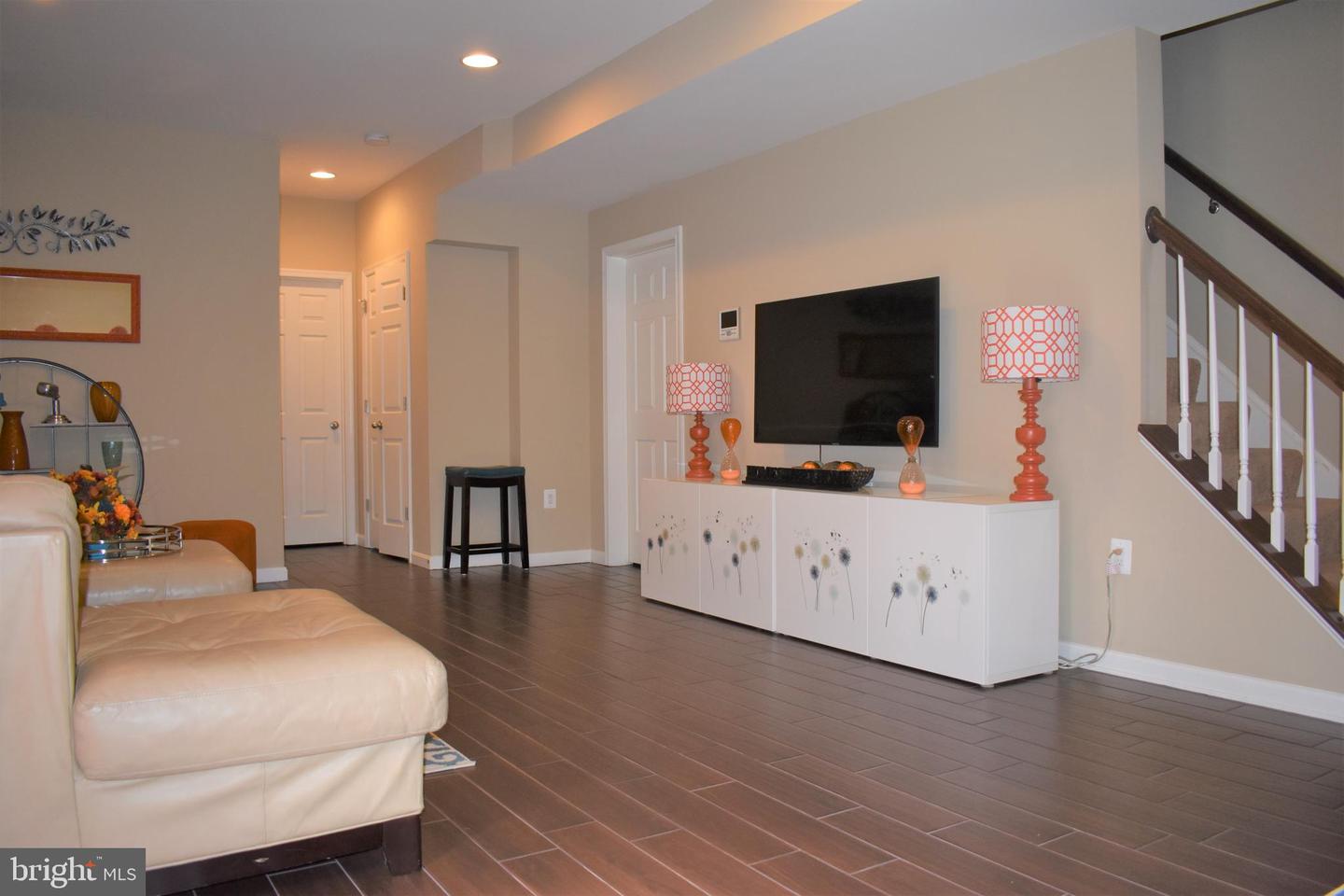 Living room with a cream sectional, dark tile floors, a white media console, and a staircase.