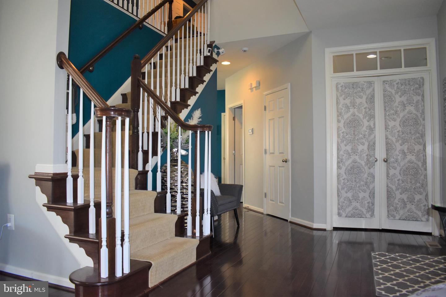 Foyer with a carpeted staircase, dark wood railing, teal accent wall, and patterned double doors.