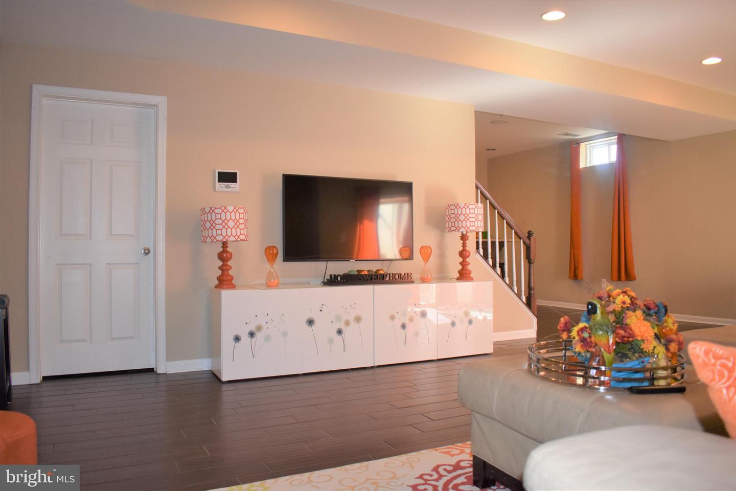 Living room with a wall-mounted television, white floral cabinet, dark tile floor, and staircase.
