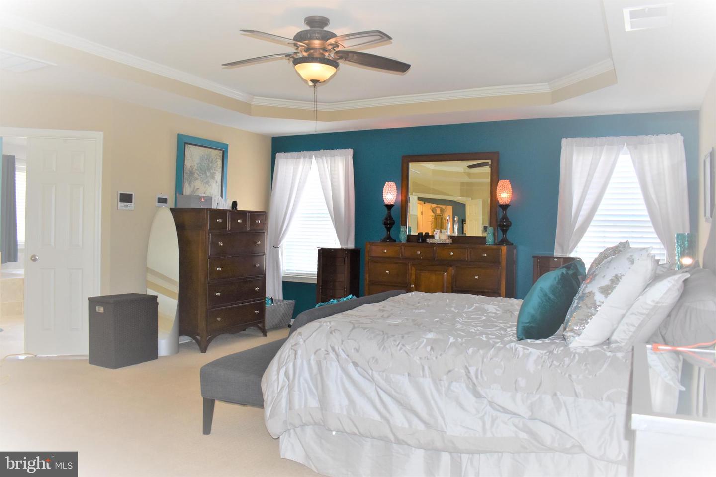 Bedroom with a teal accent wall, dark wood dressers, and a white bed beneath a tray ceiling.