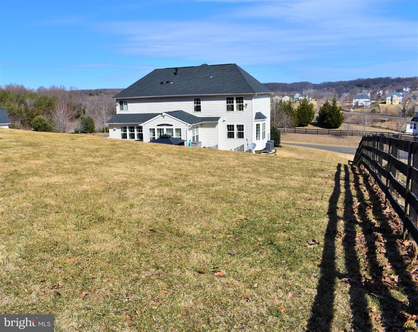 Two-story white house viewed from a sloping backyard, with a broad lawn and black fence.