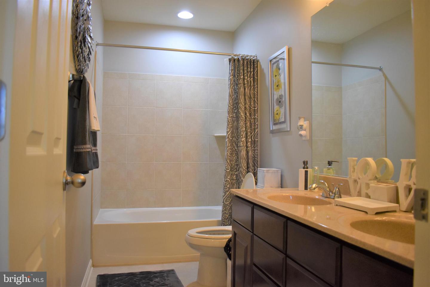 Bathroom with a tub, patterned shower curtain, and long double-sink vanity.