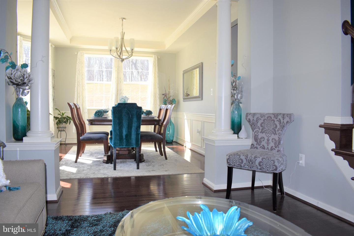 Dining room with a teal accent chair, dark wood table, chandelier, and white columns.
