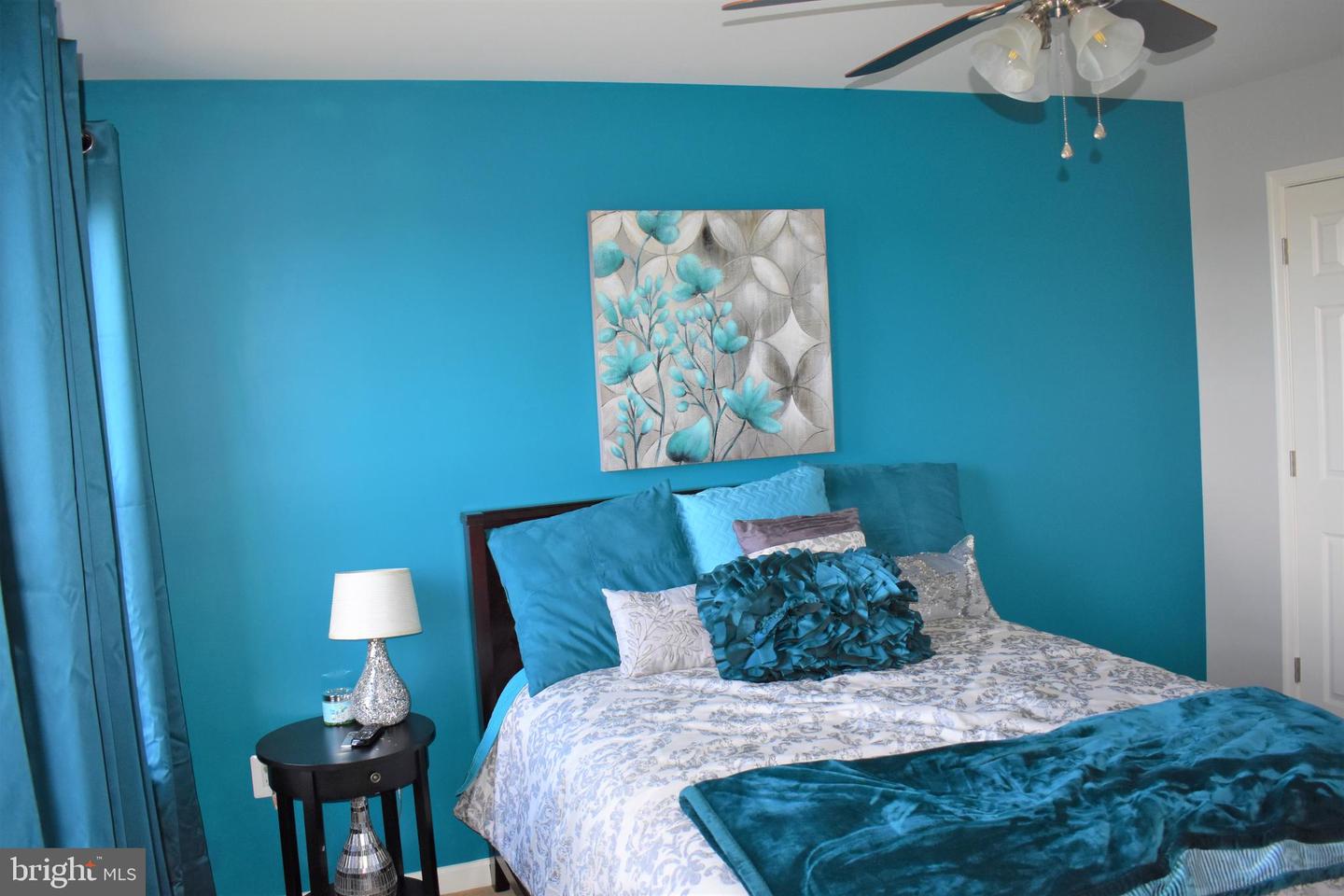 Bedroom with teal walls, patterned bedding, and floral wall art.