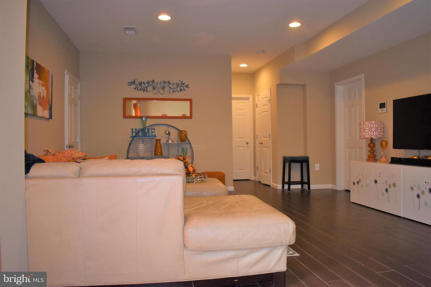 Furnished living room with a light leather sectional, ottoman, dark tile floors, and wall-mounted television.