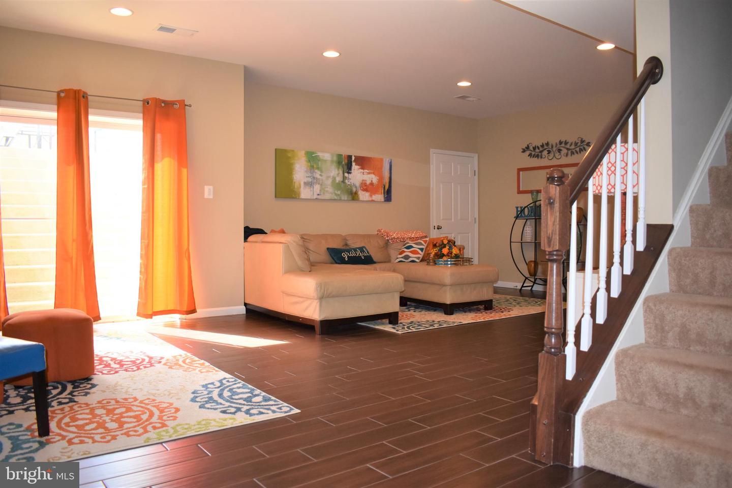 Living room with a beige sectional, colorful rugs, orange curtains, and a staircase.