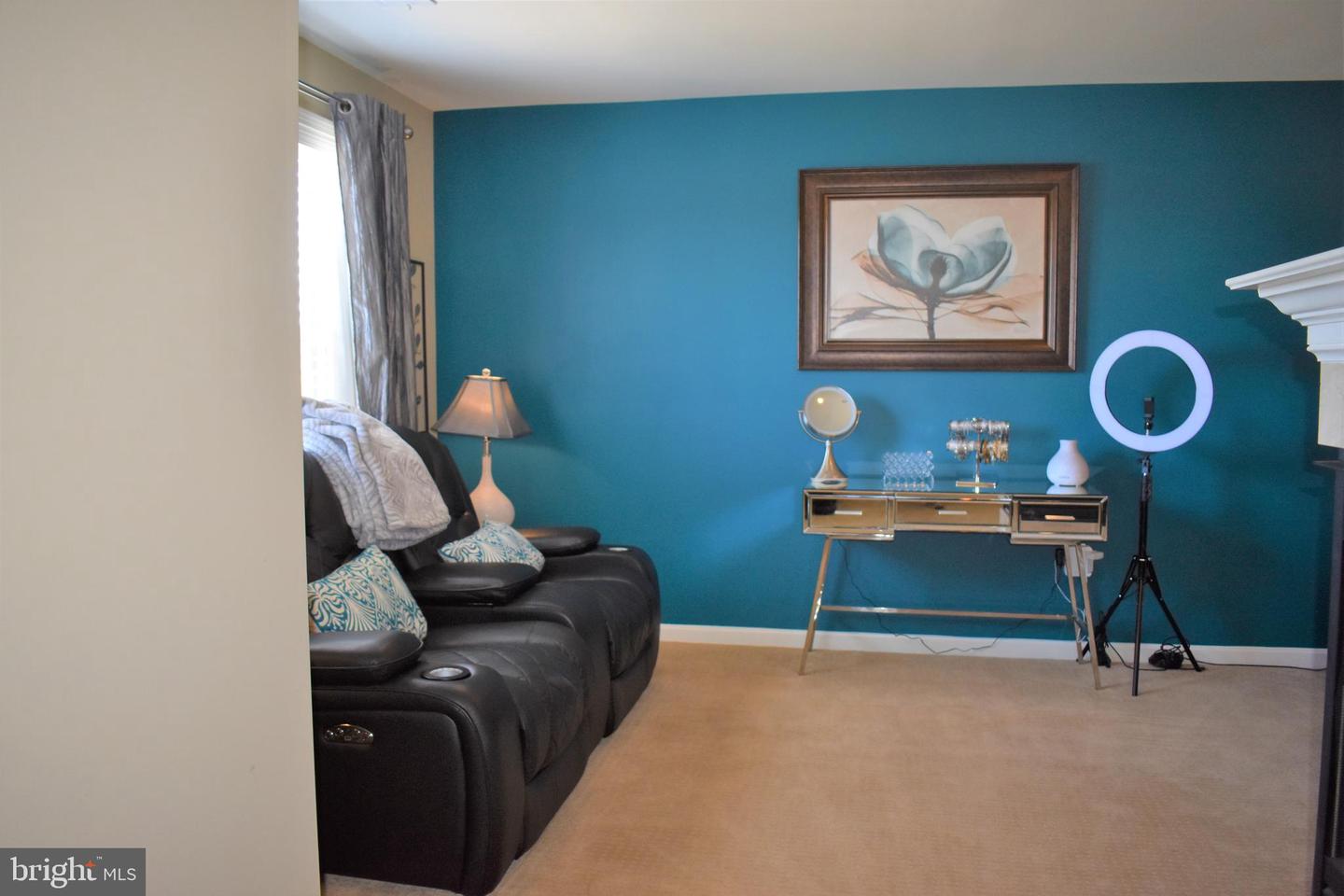 Furnished room with teal walls, a black reclining sofa, and a console table beside a ring light.