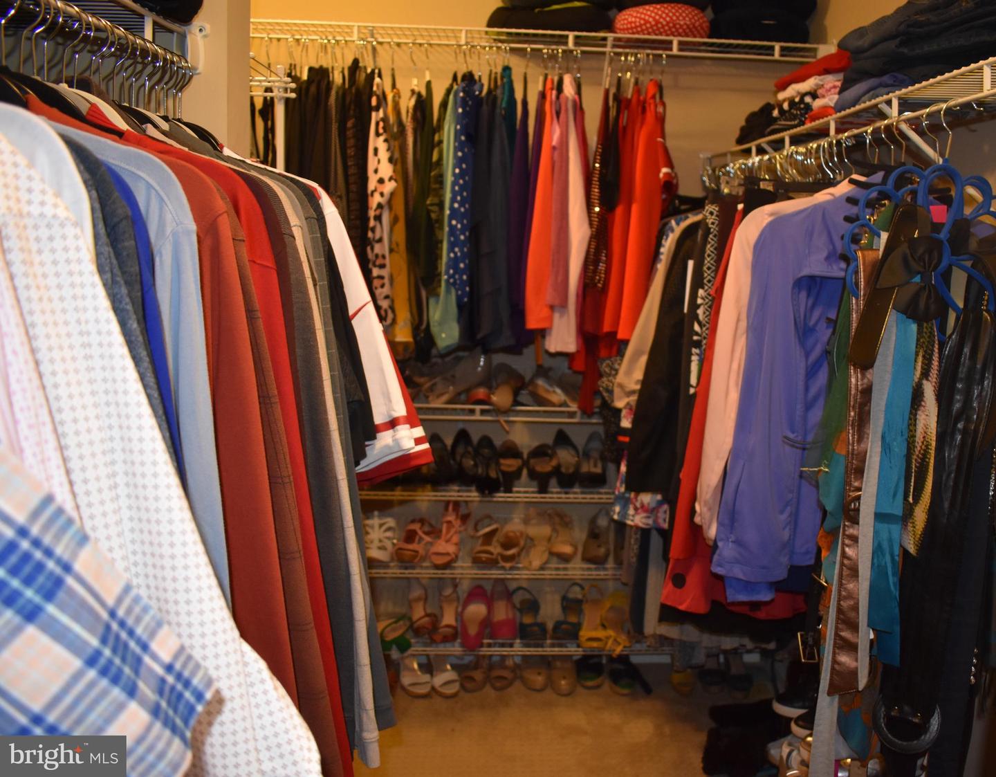 Walk-in closet with clothing racks on both sides and shelves of shoes at the back.