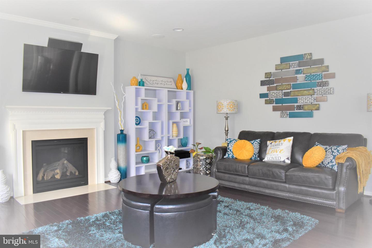 Staged living room with a white fireplace, gray leather sofa, and turquoise shag rug.