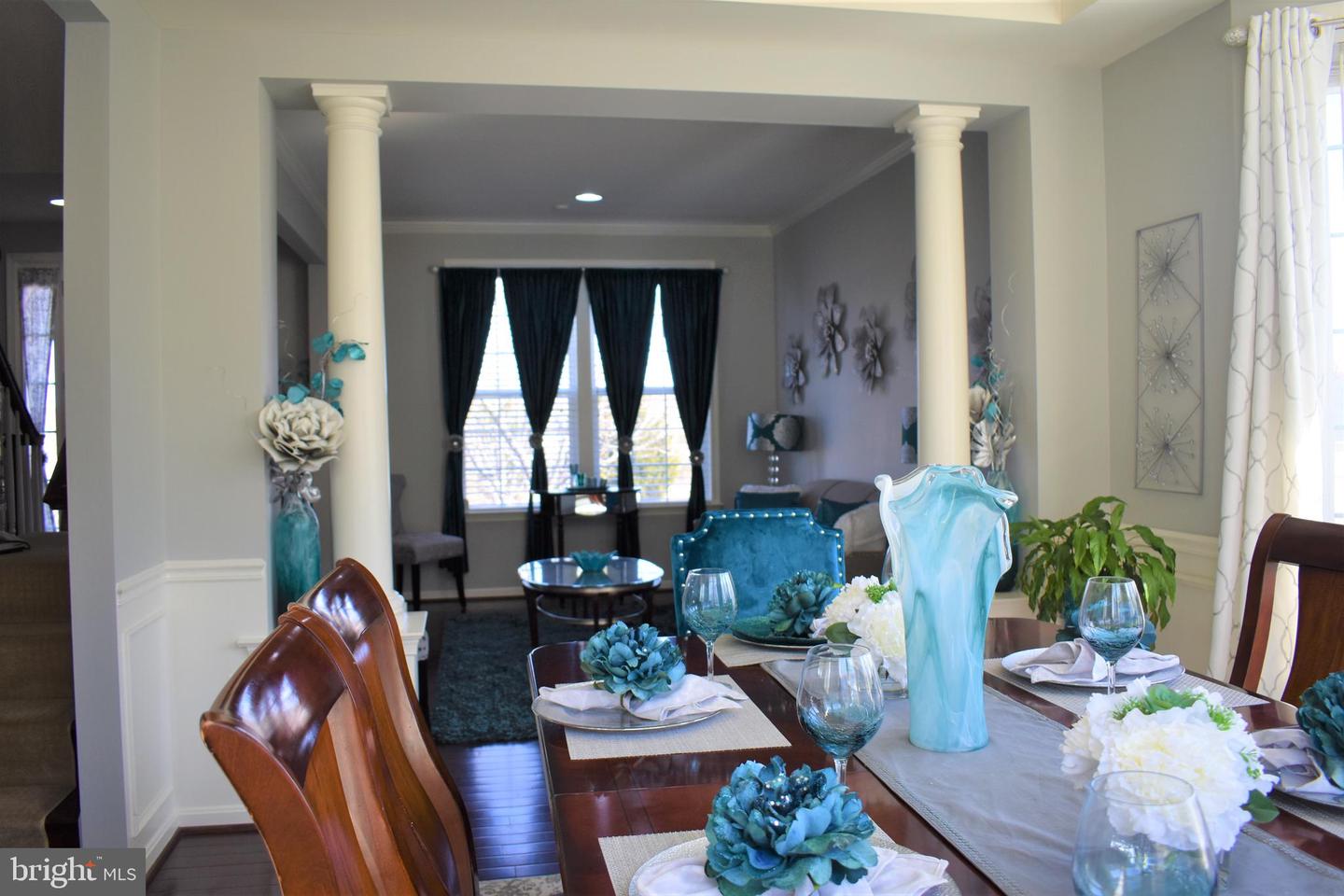 Dining room with a set table, blue floral arrangements, and white columns framing the living area.