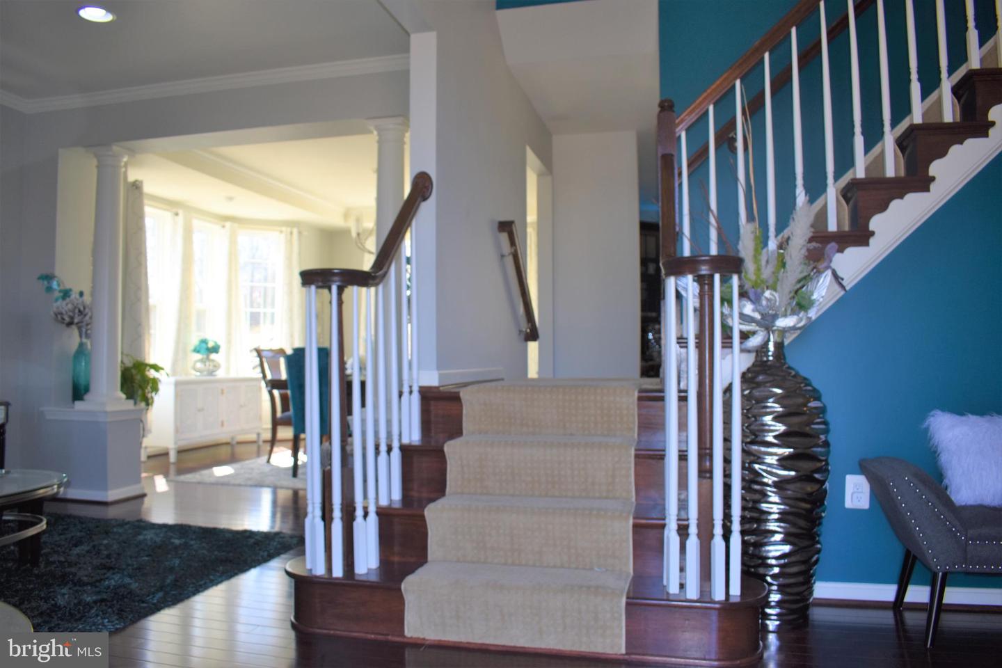 Foyer with curved wood staircase, beige carpeted steps, white balusters, and a teal accent wall.
