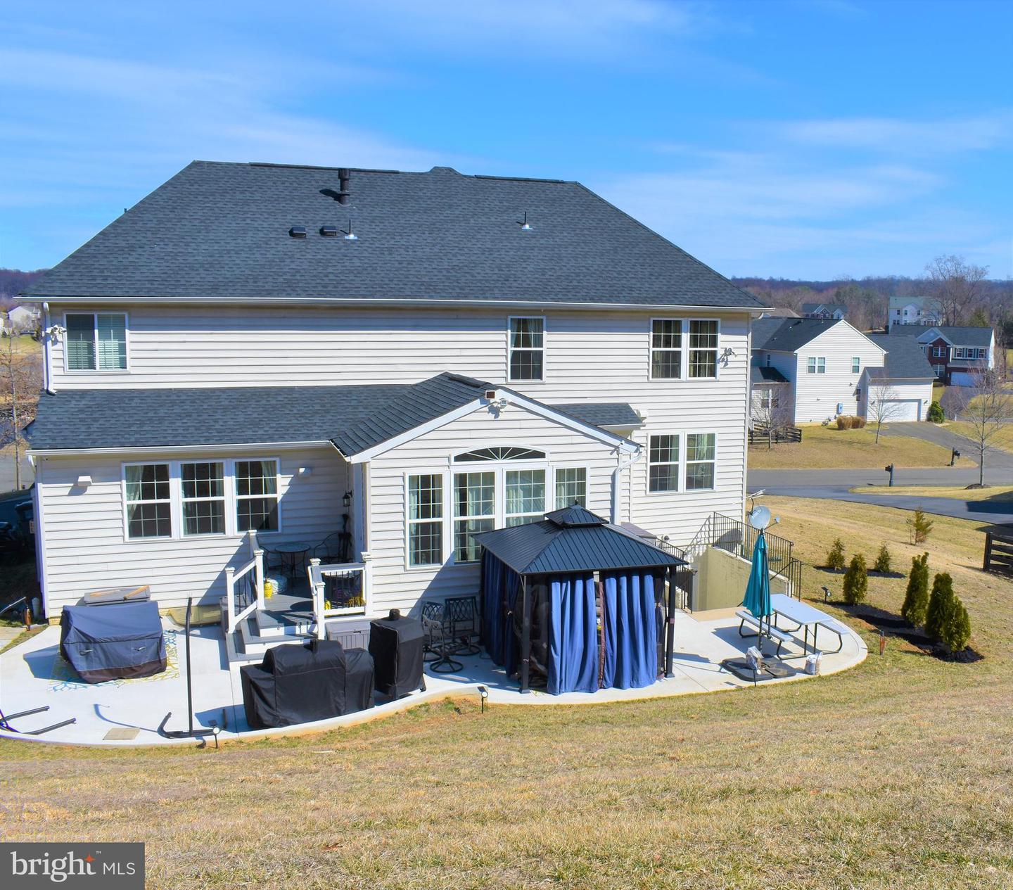 Rear of a two-story home with a large patio, outdoor seating, and a curtained gazebo.