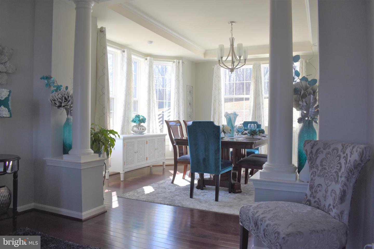 Furnished dining room with blue chairs, a dark wood table, white columns, and large curtained windows.